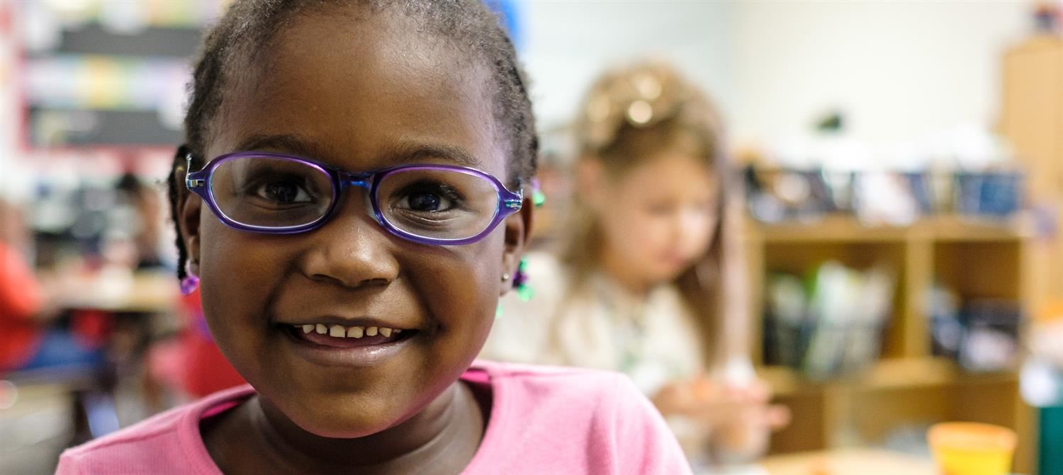 Girl smiling with another girl working in the background 